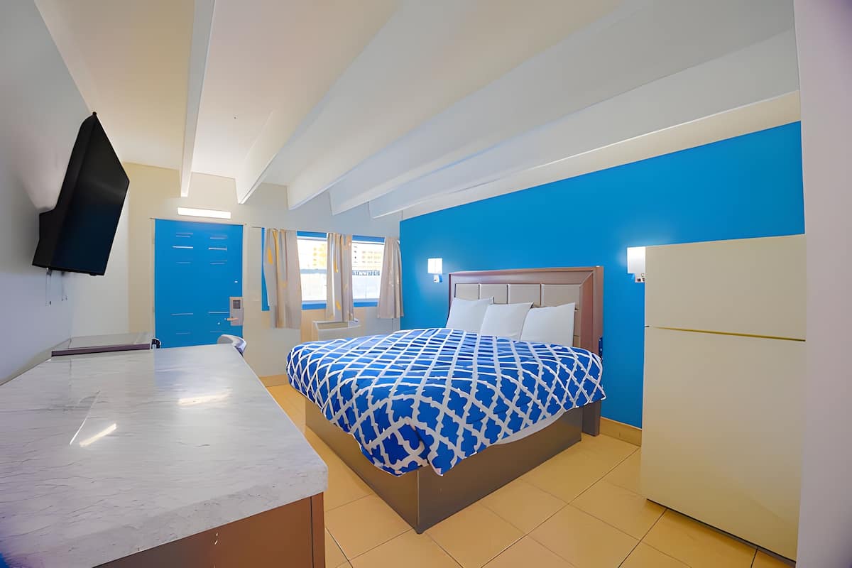 A hotel room with a bed, a desk, a television, and a blue wall.