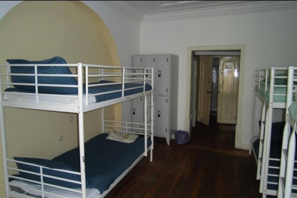 A dormitory room with bunk beds, a wardrobe, and a door leading to another room.