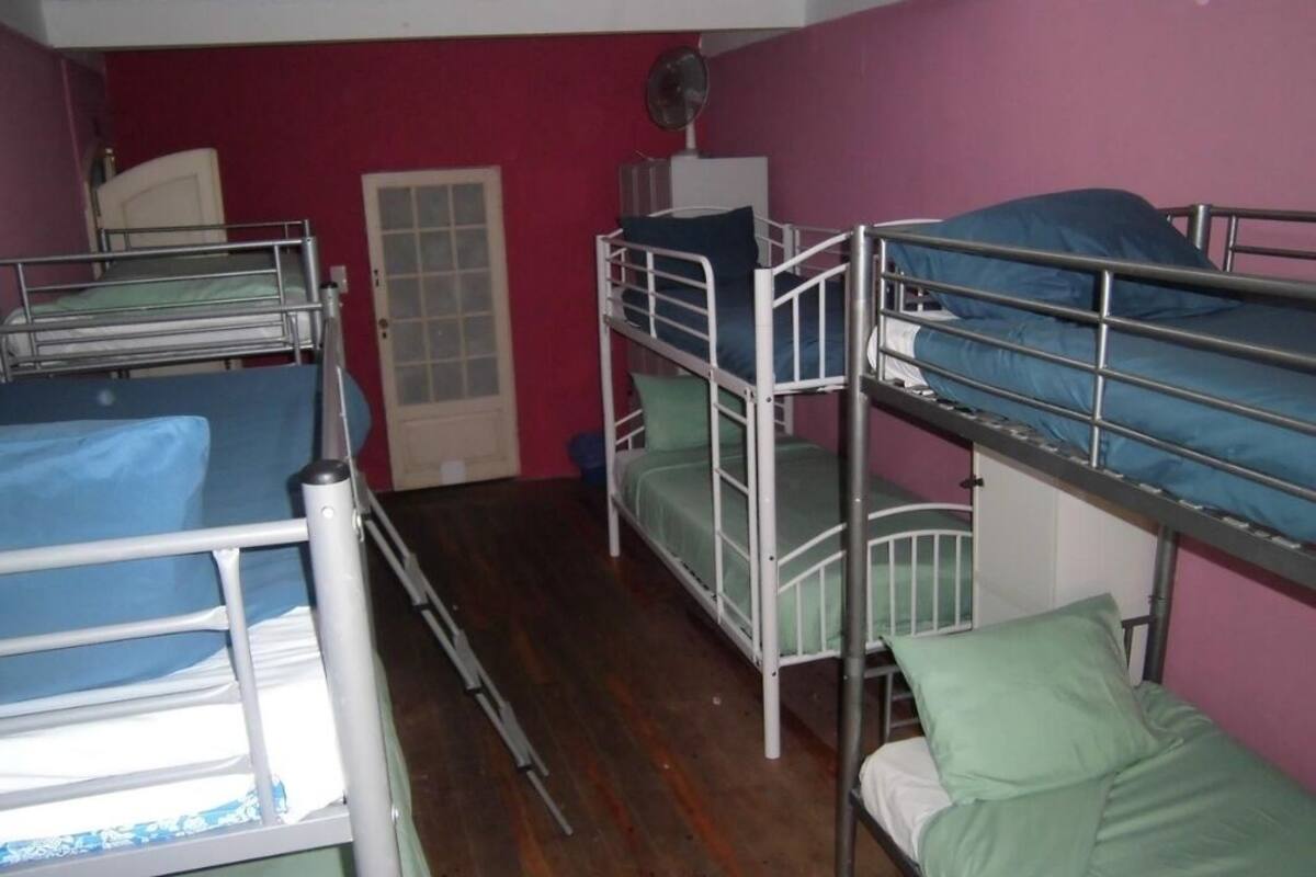 A dormitory room with bunk beds, a door, and a fan on the wall.