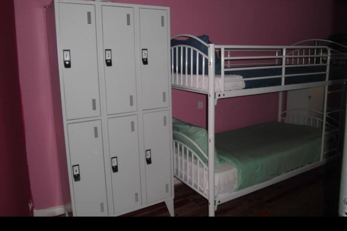 A bunk bed with a green mattress and a white metal frame, a white metal wardrobe with multiple compartments, and a pink wall.