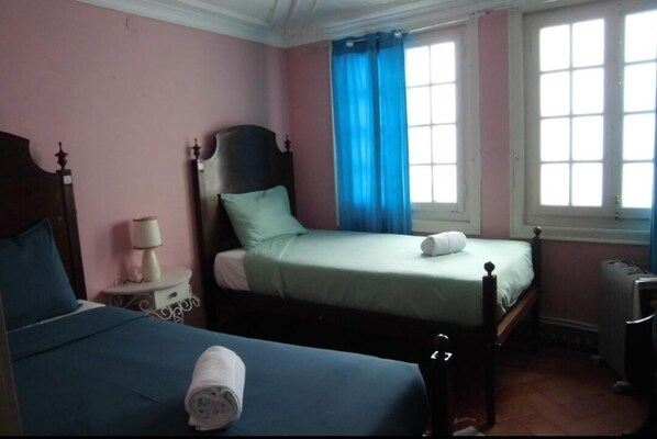 A bedroom with two beds, a nightstand, a lamp, and a window with blue curtains.