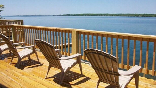 A wooden deck with four Adirondack chairs facing a calm lake. - Cottage #13 - 3 bedroom/ 1 bath (Cape Vincent)