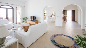 A spacious living room with a white sofa, a coffee table, and a TV. There are archways leading to other rooms.
