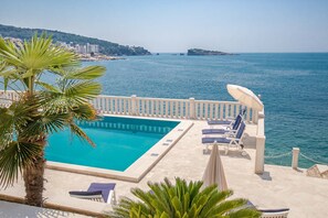 Un espace aménagé au bord de la piscine, avec vue sur la mer, comprenant des chaises longues et un palmier.