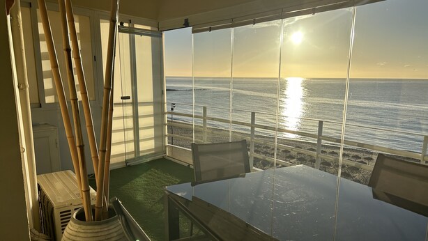 A balcony with a view of the ocean at sunset, a glass table, and chairs. - BEACHFRONT APARTMENT IN FUENGIROLA (Fuengirola)