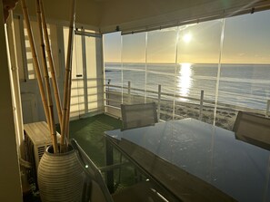 A balcony with a view of the ocean at sunset, a glass table, and chairs. - BEACHFRONT APARTMENT IN FUENGIROLA (Fuengirola)