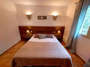 Comfortable room with a neatly made bed, bedside tables, and a headboard, featuring a framed picture and a window with curtains.