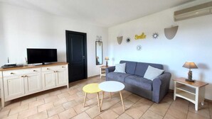 A living room with a grey sofa, a TV on a wooden cabinet, a small round table, and a lamp on a side table.