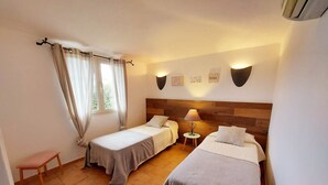 A room with two single beds, a small table, a chair, and a window with curtains.