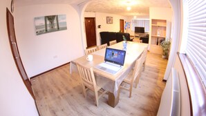 A dining area with a wooden table, chairs, and a laptop. There is a white wall with a framed picture and a door in the background. - College Street Abode - Guest House (Portsmouth)