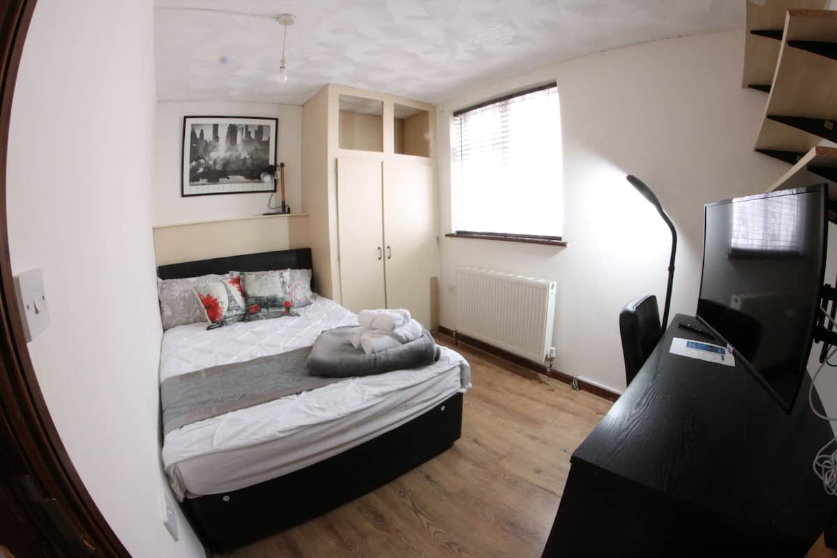 Ein Schlafzimmer mit Bett, Schreibtisch, Stuhl, Heizkörper und einem Fenster mit Jalousien.