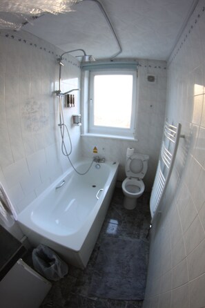 A small, compact bathroom with a bathtub, toilet, and a window. - College Street Abode - Guest House (Portsmouth)