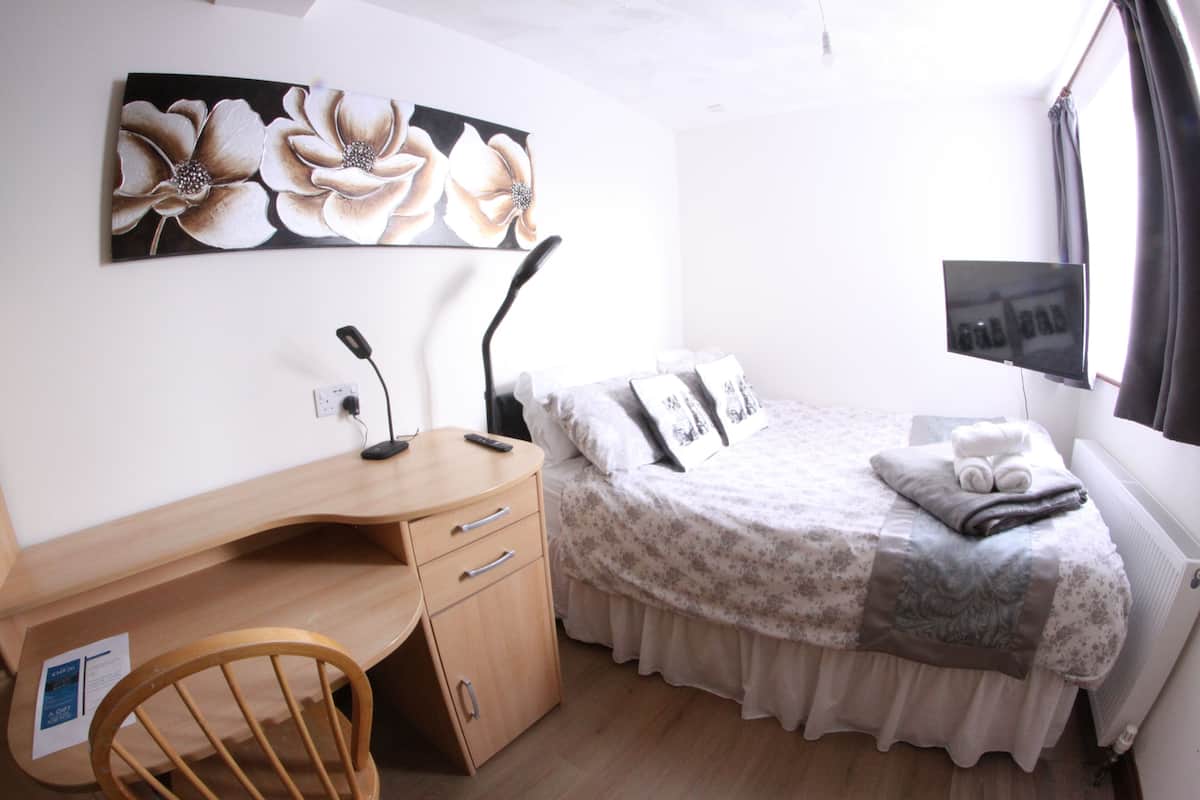 Ein Schlafzimmer mit Bett, Schreibtisch, Stuhl, Heizkörper und einem an der Wand befestigten Fernseher.