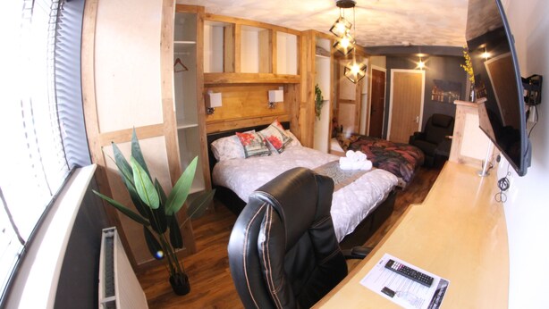 A bedroom with a bed, a desk, a chair, a potted plant, and a television. - College Street Abode - Guest House (Portsmouth)