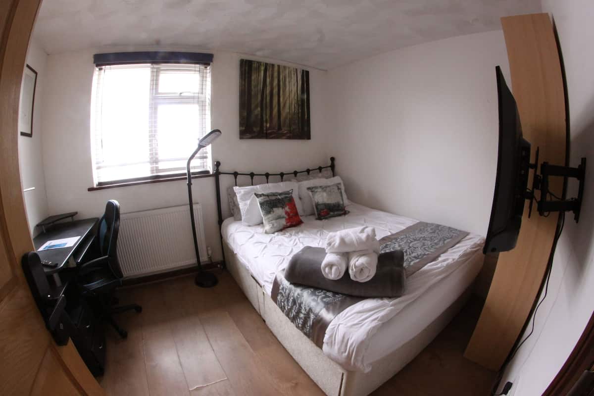 Ein Schlafzimmer mit Bett, Schreibtisch, Stuhl, Fenster und einem Bild an der Wand.