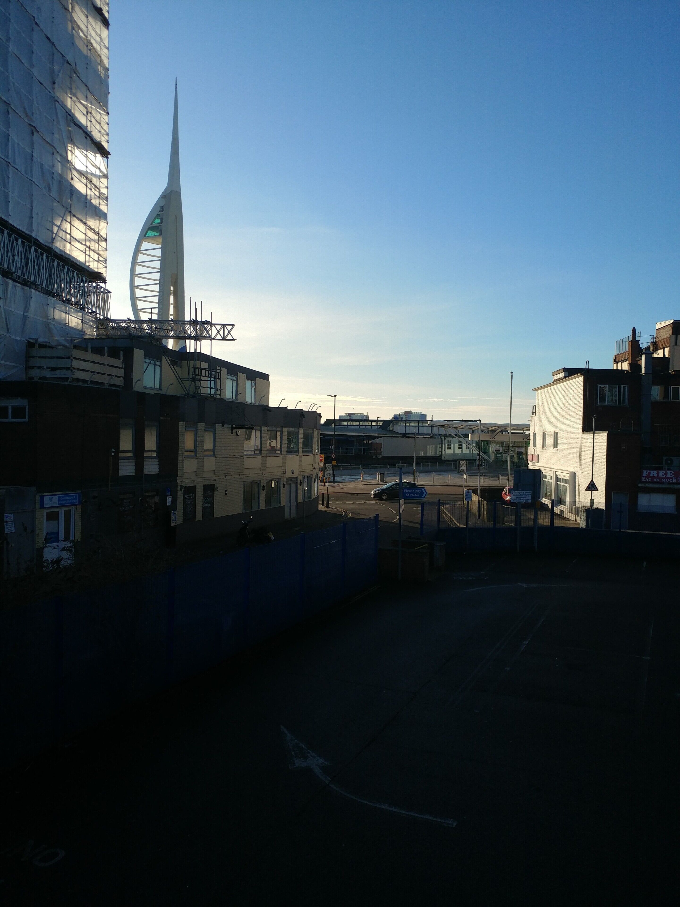 A view of a cityscape with a prominent tower and a circular building, surrounded by modern buildings and a clear sky.
