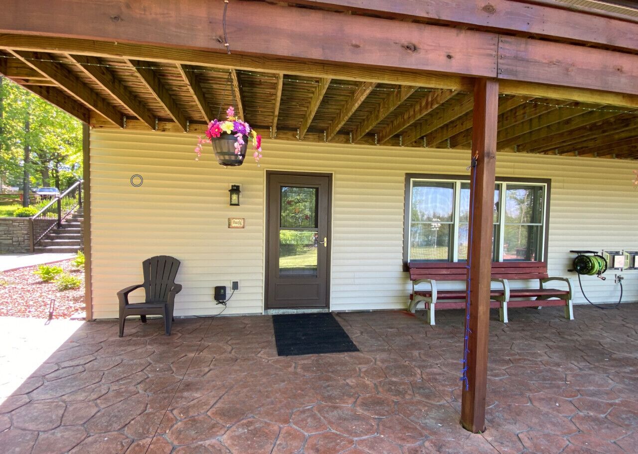 A covered porch with a wooden ceiling, a door, and a bench.