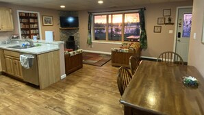 A spacious kitchen with wooden cabinets, a dining table, and a large window offering a view of the outdoors. - Hidden Charm Suites - Peaceful Suite Lake Retreat (Lapeer)