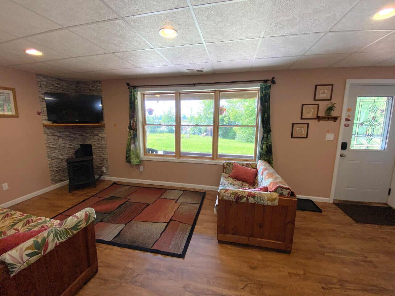A living room with a stone fireplace, a large window with curtains, and a door with a glass panel.