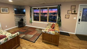 A living room with a stone fireplace, a large window with curtains, and a door with a mailbox. - Hidden Charm Suites - Peaceful Suite Lake Retreat (Lapeer)