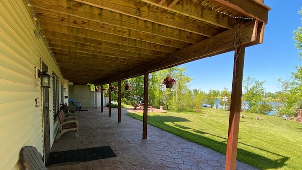 A covered patio with stone flooring, wooden benches, and hanging flower baskets. - Hidden Charm Suites - Peaceful Suite Lake Retreat (Lapeer)