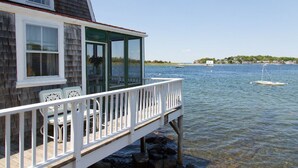 A wooden deck with white railings and chairs, overlooking a calm body of water with boats. - Clean Waterfront Classic Cottage with Private Beach (Gloucester)