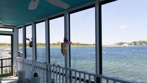 A covered deck with large windows overlooking a body of water, featuring a flag and a lifebuoy. - Clean Waterfront Classic Cottage with Private Beach (Gloucester)