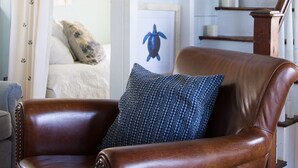 A room with a brown leather armchair, a blue patterned pillow, and a staircase with a wooden railing. - Clean Waterfront Classic Cottage with Private Beach (Gloucester)