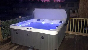 A hot tub on an outdoor deck with a wooden railing and a backdrop of trees and a sunset sky. - 3 bedroom accommodation in Otterburn (Otterburn)