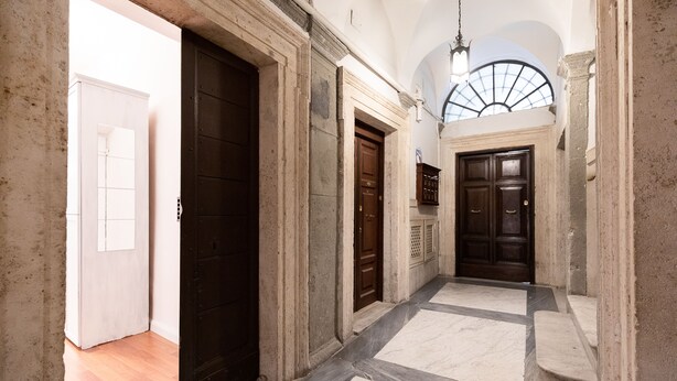 Un couloir avec une porte en bois, une porte blanche et un escalier menant à l’étage supérieur.