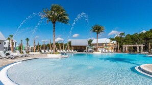 A large outdoor swimming pool with clear blue water, surrounded by palm trees and lounge chairs.