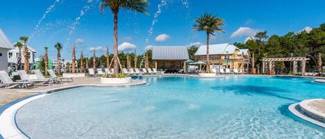 A large outdoor swimming pool with clear blue water, surrounded by palm trees and lounge chairs.
