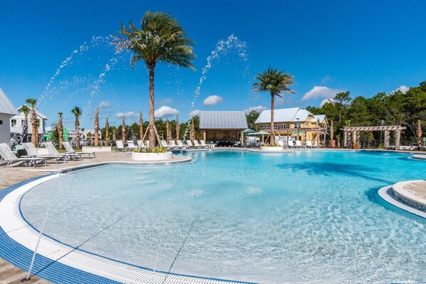 A large outdoor swimming pool with clear blue water, surrounded by palm trees and lounge chairs. - Steps To Pool - Prominence 30A "Sand By Me" 4BR/4.5BA, Sleeps 14, Bikes, The Hub (Inlet Beach)
