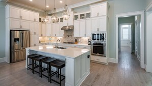 A modern kitchen with white cabinetry, a central island with bar stools, stainless steel appliances, and pendant lighting.