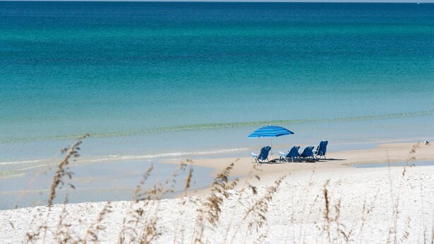 A beach with clear turquoise water, a sandy shore, and a blue umbrella providing shade.