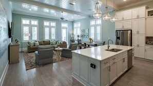 A spacious living area with a large sofa, a dining table, and a kitchen with white cabinets and stainless steel appliances.