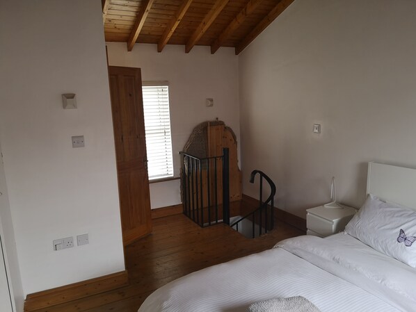 A bedroom with a wooden ceiling, a bed with white bedding, a nightstand, and a window with blinds.
