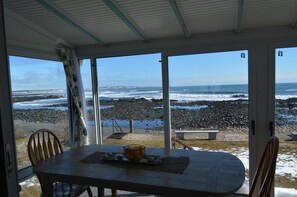 Une pièce avec une table et des chaises, une vue sur la plage et un banc à l’extérieur.