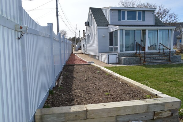 A residential property with a fenced yard, a raised garden bed, and a house with a porch.