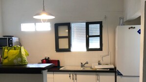 Una cocina compacta con armarios blancos, encimera negra, refrigerador blanco y una ventana con persianas.