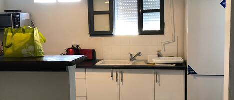 Uma cozinha compacta com armários brancos, bancada preta, geladeira branca e janela com persianas.