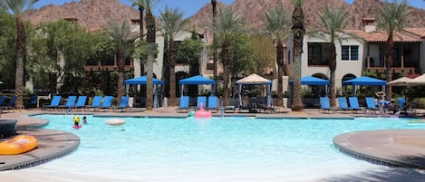 A pool area with lounge chairs and umbrellas, surrounded by palm trees and buildings.
