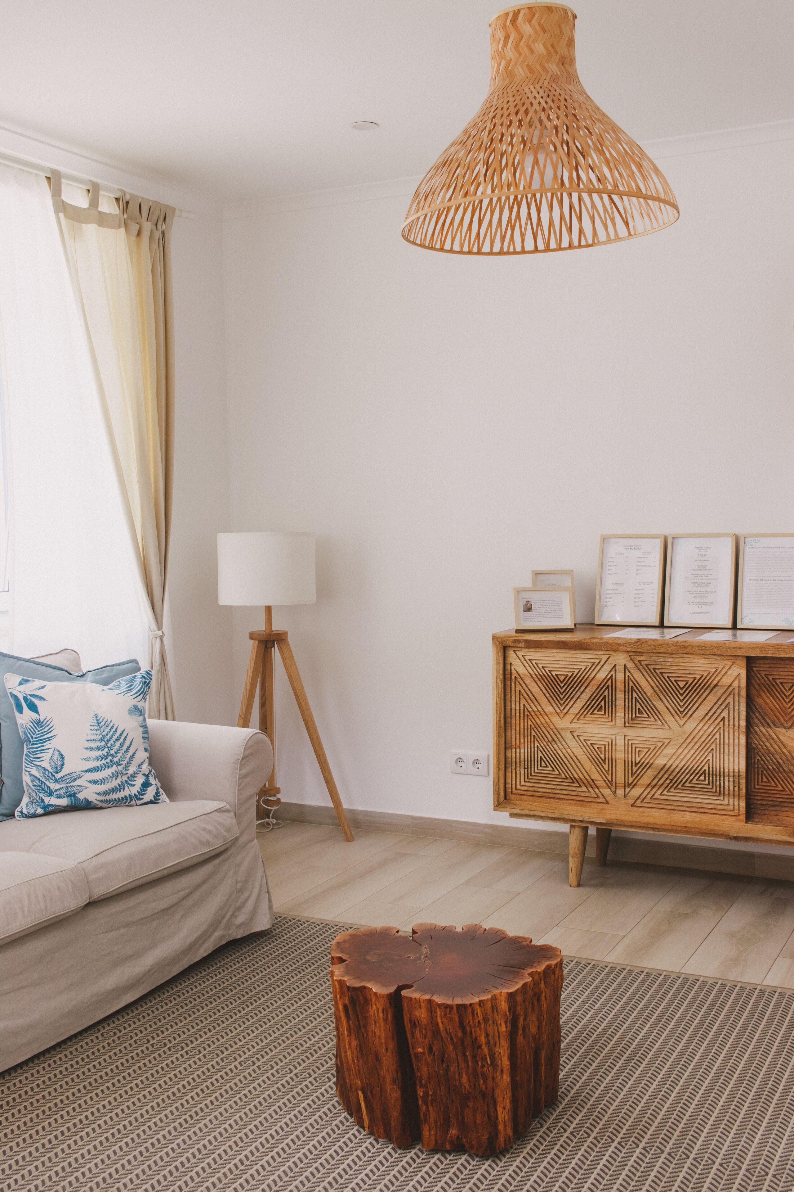 Ein Wohnzimmer mit einer Couch, einer Holzkommode, einer Stehlampe und einer gewebten Pendelleuchte.