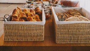 A kitchen with a wooden table displaying bread and pastries, a microwave, and a shelf with kitchen items.