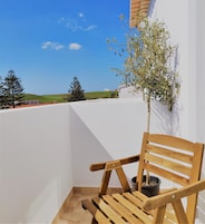 Ein Holzstuhl mit einem Blumentopf auf einem Balkon mit weißer Wand, mit Blick auf eine grüne Landschaft.