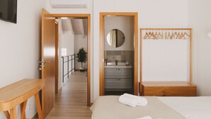 A hotel room with a wooden bed, a bedside table, a mirror, a wardrobe, and a bathroom visible through an open door.
