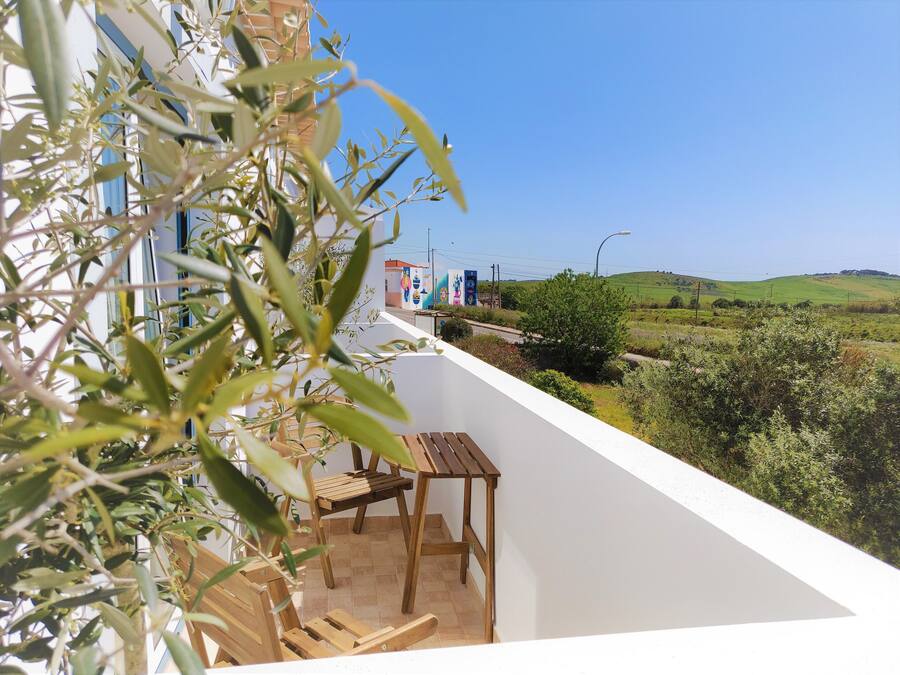 Un balcón con mesa y sillas de madera, con vistas a un paisaje verde y un edificio con murales coloridos.