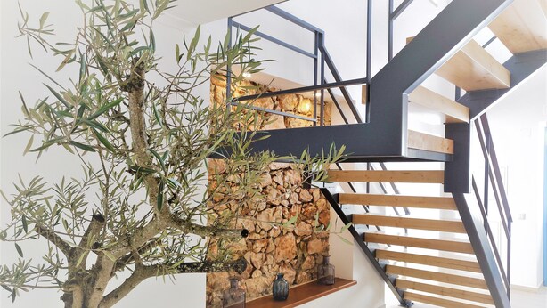 A modern staircase with wooden steps and black metal railings, leading to a landing with a stone wall and a tree.