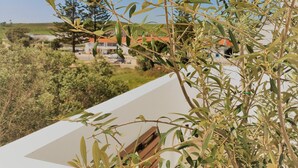 A balcony with olive trees, a clear blue sky, and a view of houses in the distance.