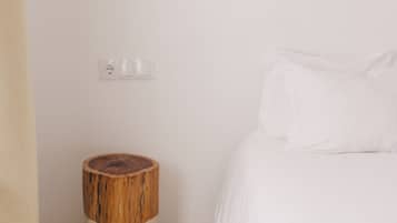 A minimalist bedroom with a wooden stool, a bedside table, and a wall-mounted light fixture.